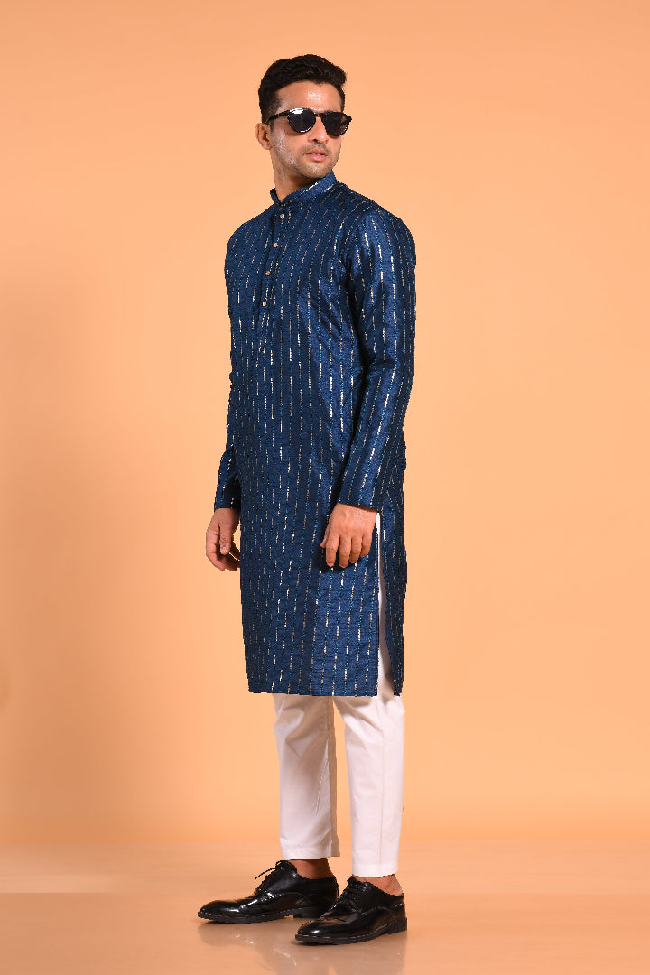 This Teal Blue silk-blend kurta is designed for comfort and elegance, featuring tone-on-tone threadwork with sequin detailing that runs horizontally for a striking yet subtle effect. Ideal for pujas, haldi, and festive occasions, the kurta is adorned with meenakari buttons along the front placket and finished with a mandarin collar. The knee-length hem adds to its traditional charm, making it a versatile choice for special celebrations.