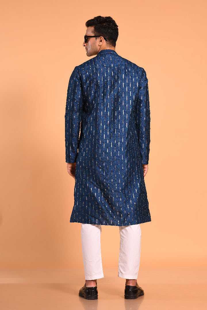 This Teal Blue silk-blend kurta is designed for comfort and elegance, featuring tone-on-tone threadwork with sequin detailing that runs horizontally for a striking yet subtle effect. Ideal for pujas, haldi, and festive occasions, the kurta is adorned with meenakari buttons along the front placket and finished with a mandarin collar. The knee-length hem adds to its traditional charm, making it a versatile choice for special celebrations.