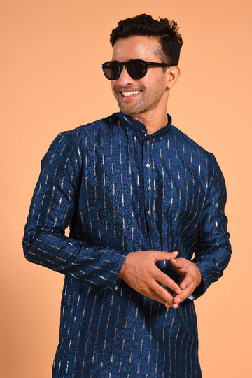 This Teal Blue silk-blend kurta is designed for comfort and elegance, featuring tone-on-tone threadwork with sequin detailing that runs horizontally for a striking yet subtle effect. Ideal for pujas, haldi, and festive occasions, the kurta is adorned with meenakari buttons along the front placket and finished with a mandarin collar. The knee-length hem adds to its traditional charm, making it a versatile choice for special celebrations.