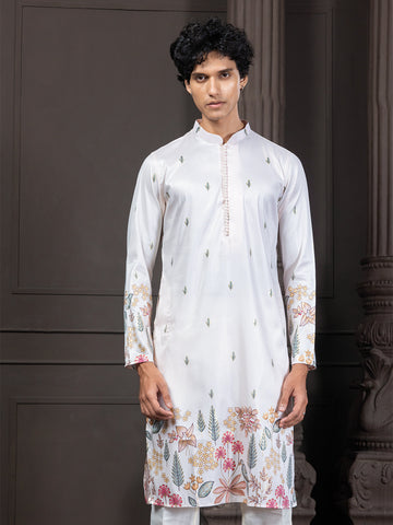 Man wearing a white kurta with floral patterns against a dark background